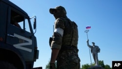 Військова вантажівка з літерою Z, яка стала символом російської армії, проїжджає повз російського солдата, який стоїть на дорозі на в’їзді до Маріуполя, червень 2022 року