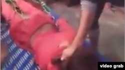 The video shows a man pinning the transgender woman face down on a bed with his foot and beating her bare buttocks with a belt.